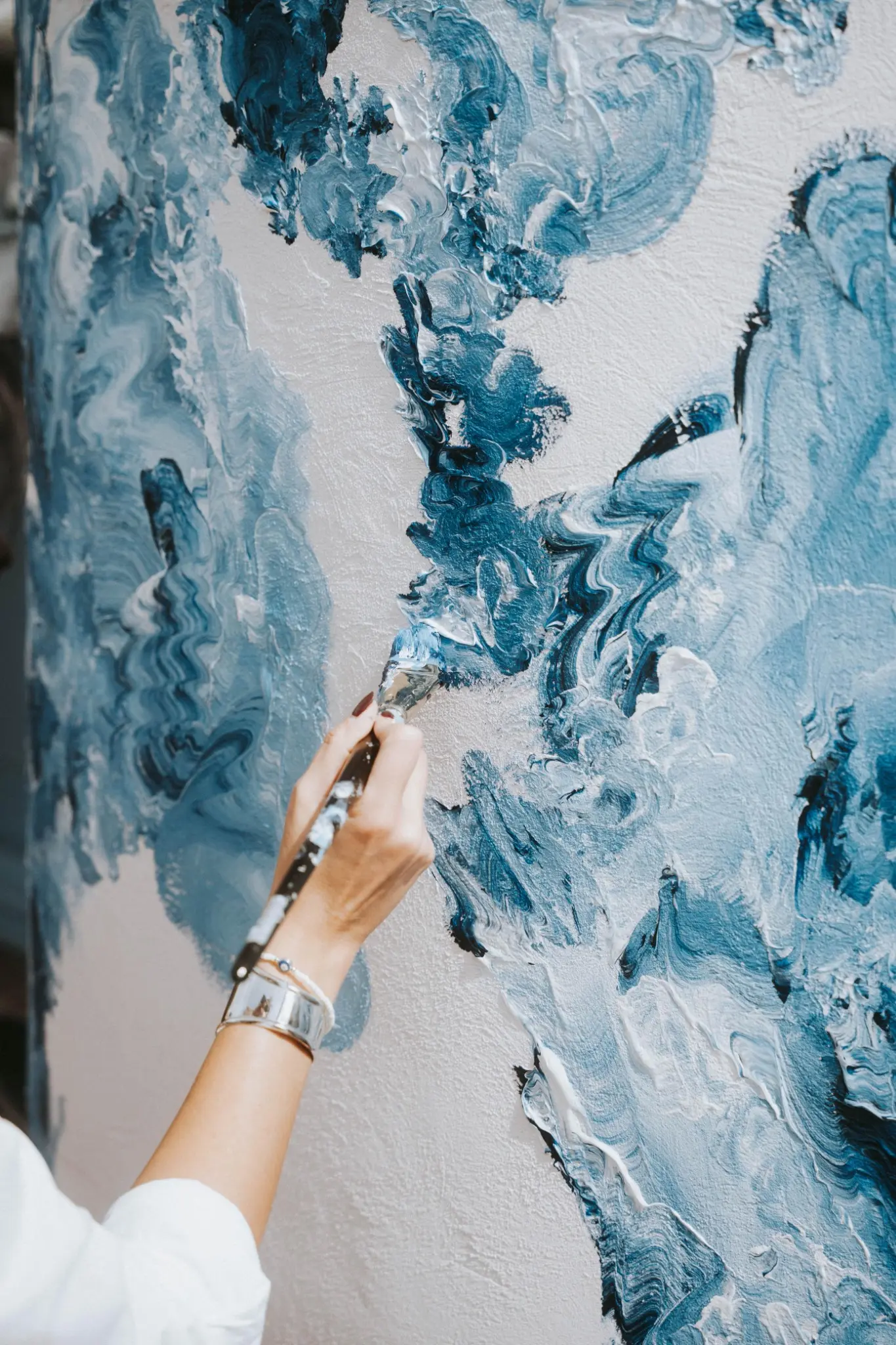 The artist’s hand applying paint with a brush.